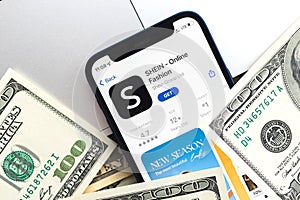 Shein shopping app logo on mobile phone screen. Business background with laptop and money photo