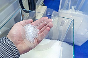 Polypropylene granules in a man's hand, against the background of production equipment for the manufacture of