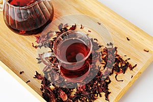 Pomegranate flowers tea in glass cup closeup. Teapot in the background. Bamboo tray with scattered petals. Ruby infusion