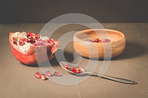 Pomegranate fruit and grains in a wooden bowl and a spoon/Pomegranate fruit and grains in a wooden bowl and a spoon against a dark