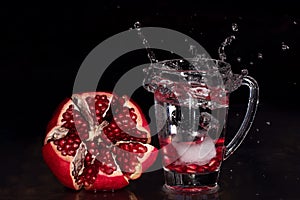 Pomegranate with glass and a splash of water against dark background