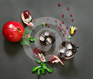 Pomegranate juice, fruit, seeds, branches on dark background, top view.