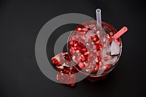 Pomegranate juice with ice, a tall glass with a cold drink and a scattering of fruit seeds on a black background
