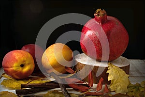 Pomegranate, nectarines and fallen leaves on a wooden background.