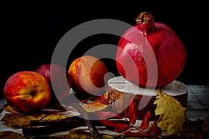 Pomegranate, nectarines and fallen leaves on a wooden background.