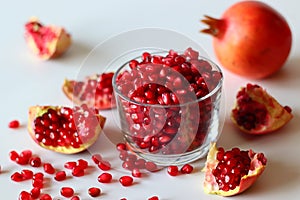 Pomegranate. Open fruit with glistening ruby red arils on a white surface, captured in soft natural light
