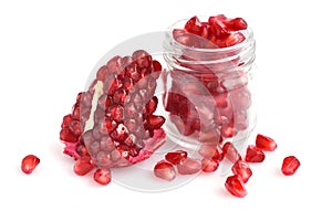 Pomegranate seeds placed in glass jar with scattered seeds on white background
