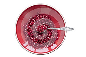 Pomegranate seeds on a red plate with a spoon on a white background