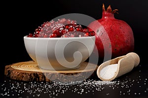 pomegranate seeds with sugar in a white bowl with black background