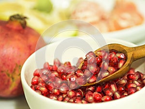 Pomegranate seeds and wooden small spoon in white bowl