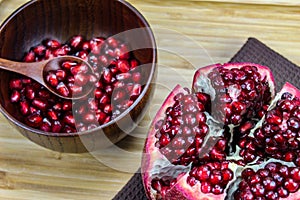 Pomegranate seeds on a wooden spoon in a bowl. Whole ripe pomegranate open on a wooden tray. Red pomegranate fruit seeds in a