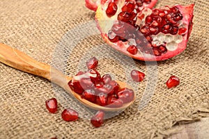 Pomegranate seeds in a wooden spoon and pieces of ripe pomegranate on a background of rough homespun fabric. Close up