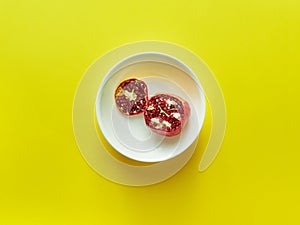 Pomegranate sliced in white bowl viewed from above over a yellow background