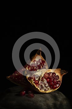 Pomegranate still life - two quarter of a pomegranate and grains on a black background