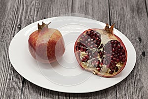 Pomegranates have broken into pieces with red berries on a porcelain plate on a dark background.