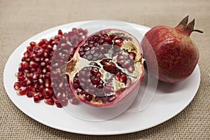 Pomegranates have broken into pieces with red berries on a porcelain plate on a textile background.