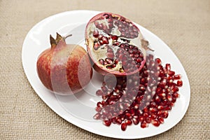 Pomegranates have broken into pieces with red berries on a porcelain plate on a textile background.