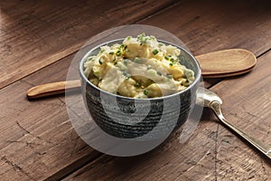 Pomme puree, a photo of a bowl of mashed potatoes with herbs on a rustic background with a wooden spoon