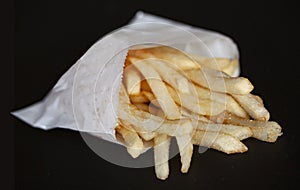 Pommes frites potatoes fries in a little white paper bag isolated on black