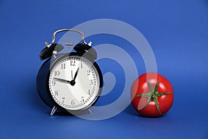 Pomodoro Technique concept - tomato and alarm clock  on blue background