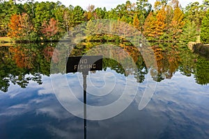 A Pond in Autumn with Reflections of Trees and No Fishing Sign.