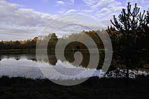 Pond in autumn with sunrise over background of frozen water, trees in November colors with blue sky and cloud