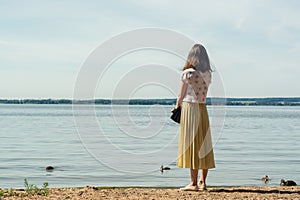 Pond beach. lonely girl in a yellow and a white blouse stands on the beach and looks into the distance.