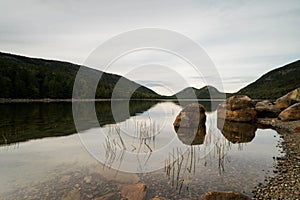 Pond with reeds and rocks and forested hills in the background