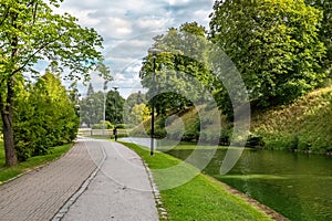 A pond in Snelli park, Tallinn, Estonia. Green trees and sidewalk on summer day with clouds