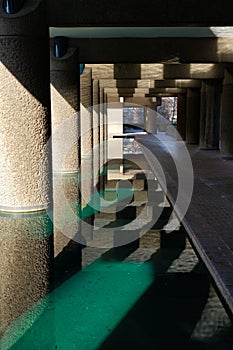 Pond and walkway under apartment block. The BarbicanEstate, City of London.