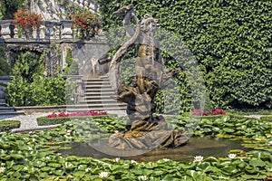 Pond with water lilies and a fountain between decorative shrubs and flowers.