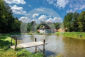 Pond with wooden pier and old house in summer landscape