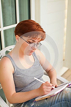 Pondering attractive caucasian woman with pen in hand thinking on plans and writing list to do in notepad