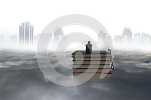 Pondering man sitting on stack of books with cityscape cloudscape