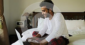 Pondering Man Using Laptop Computer Sitting On Bed Hispanic Guy Type Chatting Online In Bedroom Morning