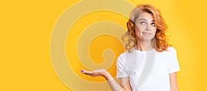 pondering redhead woman presenting product on yellow background with copy space. Beautiful woman isolated face portrait