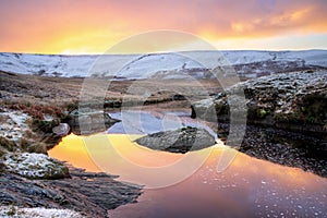 Pont Ar Elan, Elan valley, wales. Snowy scene of Afon elan flowing towards craig goch under orange sunrise with reflection of sky