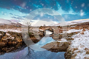 Pont Ar Elan, Elan valley, wales. Snowy scene of Afon elan flowing under a bridge with lone tree and early sun