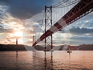 Ponte 25 de Abril Bridge in Lisbon during Sunset with ship and jesus monument, cloudy sky portugal