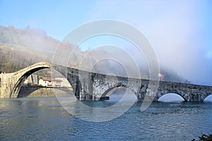 Ponte della Maddalena built in stone, called the devil`s bridge, shrouded in light fog on a cold winter morning.