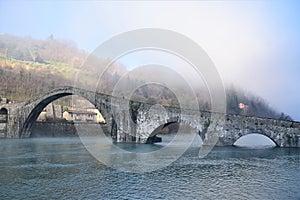 Ponte della Maddalena built in stone under a cushion of fog, called the devil`s bridge, illuminated on the left by the sun of a co