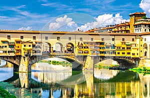 Ponte Vecchio stone bridge with colourful buildings houses over Arno River blue reflecting water in historical centre of Florence