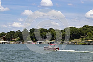 Pontoon boat motoring out past houses and boat docks on the shore on a sunny day at the lake