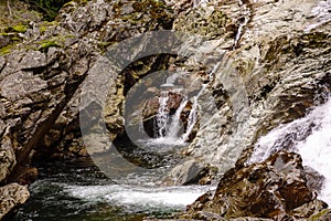 A pool at the base of a rocky waterfall in the mountains