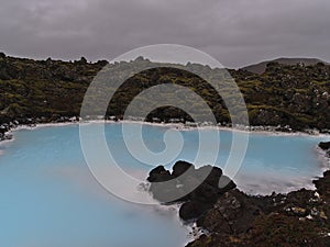 Pool with blue shimmering thermal water surrounded by moss covered lava field near spa resort Blue Lagoon in Grindavik, Iceland.