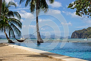 Pool and empty hammock with palm trees, isles and boats on background. Tropical beach. Philippines resort landscape.