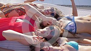 Pool party, joyful girls with beautiful figures in swimsuits waving hands hi lying on deckchair near Poolside close-up