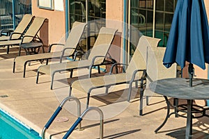 Pool side lounging chairs for sunbathing and recreation near pool with visible tables and umbrellas during the summer