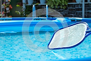 Pool Skimmer Net against clear blue water in a pool with an inflatable mattress. Round frame pool and leaf netting skimmer for