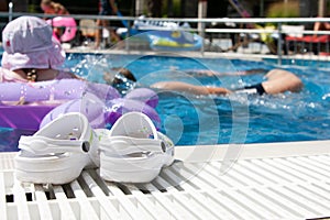 Pool and Slippers on the side. A girl swims in the background.